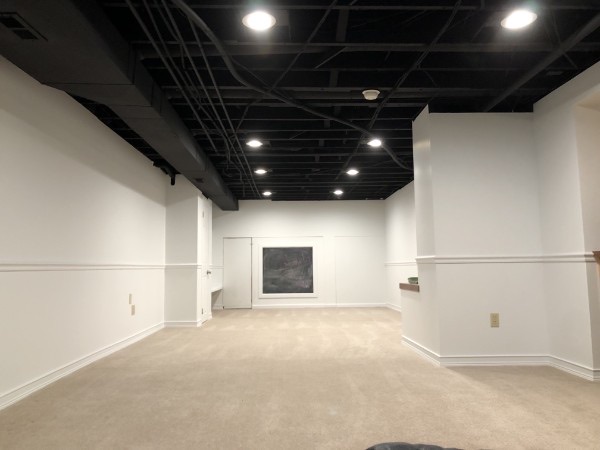 The finished basement with a black painted open ceiling, light walls, and white trim