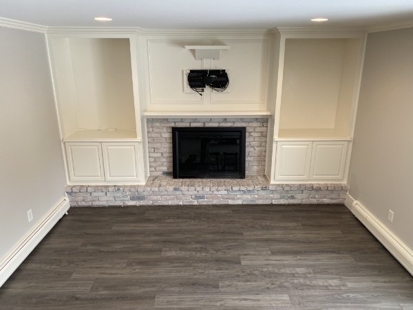 Finished room with light painted walls, white built-ins, brick fireplace, and dark flooring