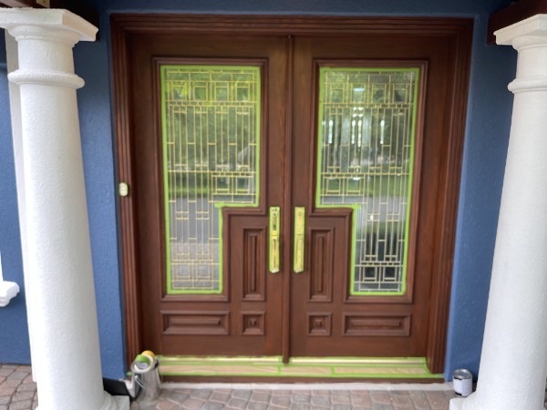 Double wood entry doors with a renewed dark finish and masking still in place